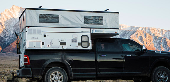 Truck camper parked on side of road with mountain background